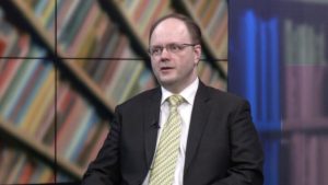 Илмарс Пойканс обсуждает пенсионный кризис в Латвии: график демографической ямы и пенсионной системы первого уровня, иллюстрирующий снижение числа работающих и угрозу будущим выплатам.