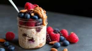 Ночная овсянка в стеклянной банке с арахисовой пастой, бананом и ягодами; полезный завтрак на тёмном фоне.