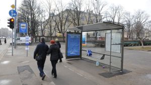 Новый павильон остановки общественного транспорта в Риге с современным стеклянным навесом и городской улицей на фоне.