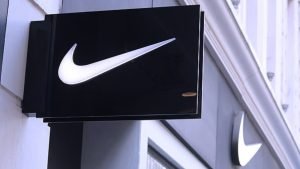 Логотип Nike на фоне магазина компании и заголовков о судебных исках против бренда в США.
